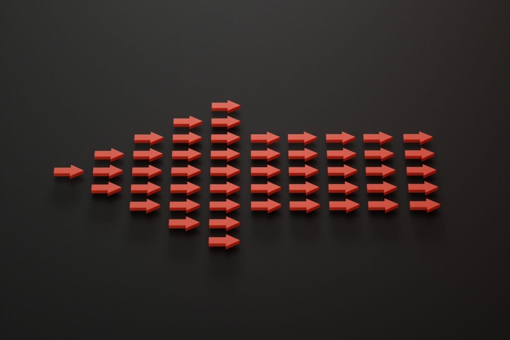 A group of red arrows on a black surface photo. Each individual arrow is pointed to right, but they as a whole shape a big arrow that points to left.